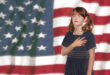 young girl in front of American flag with eyes close and hand on her heart